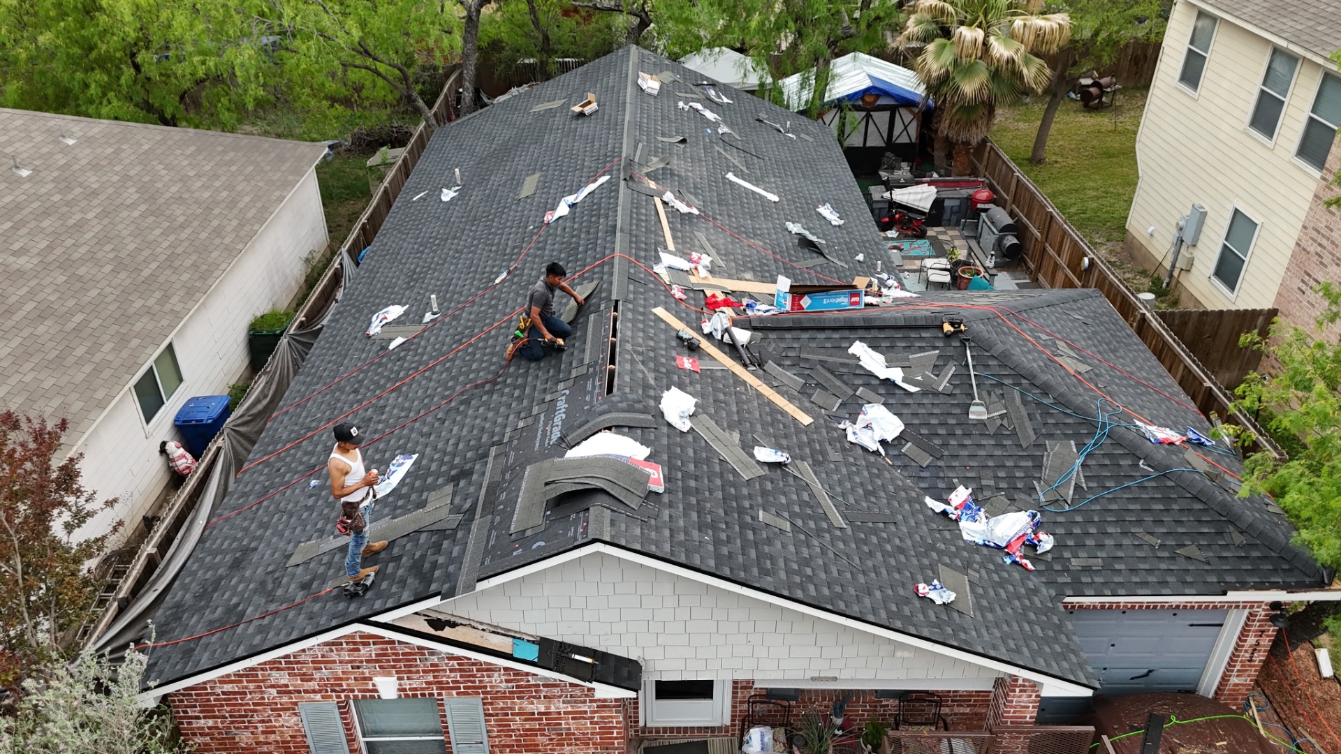 Front drone view of installers finishing hip and ridge on West Side San Antonio roof
