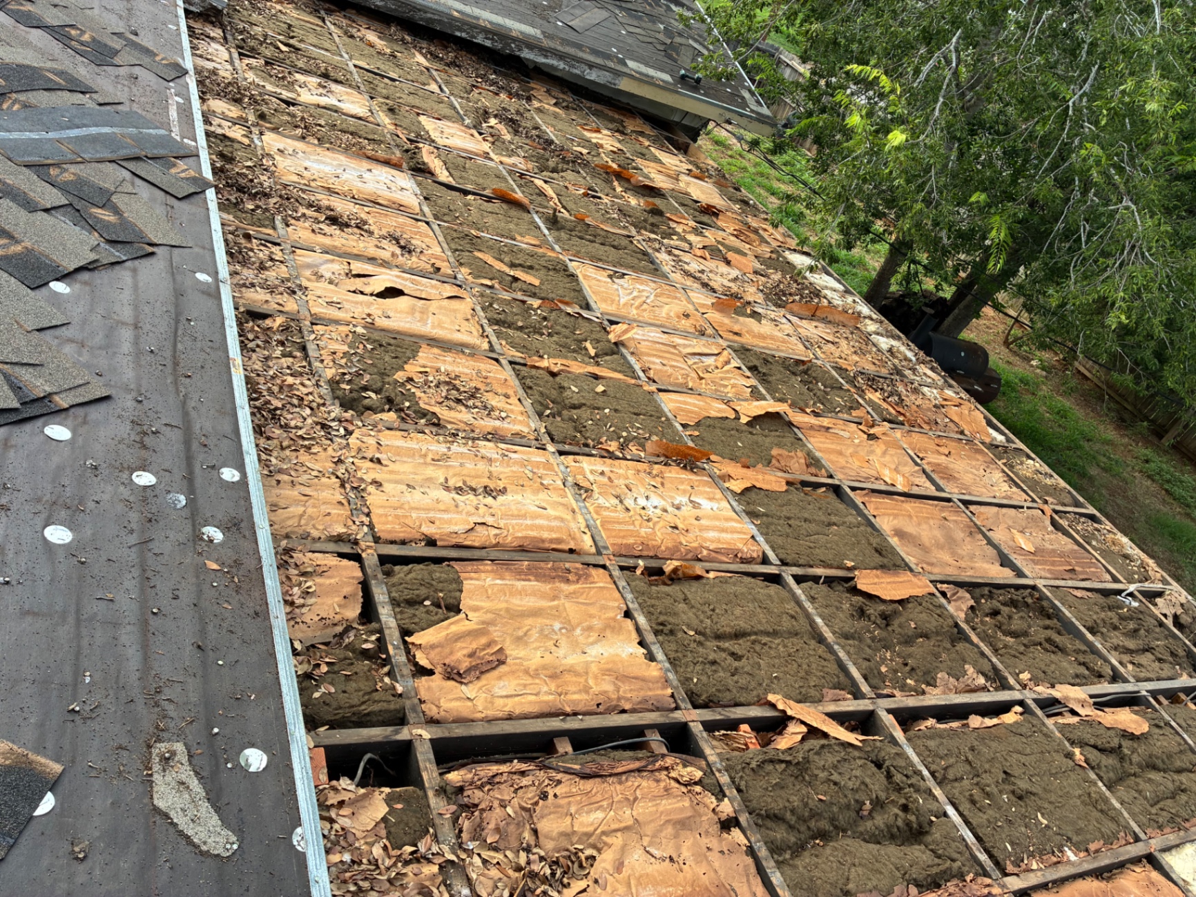 Close-up of aged decking and exposed insulation during Pearsall roof tear-off