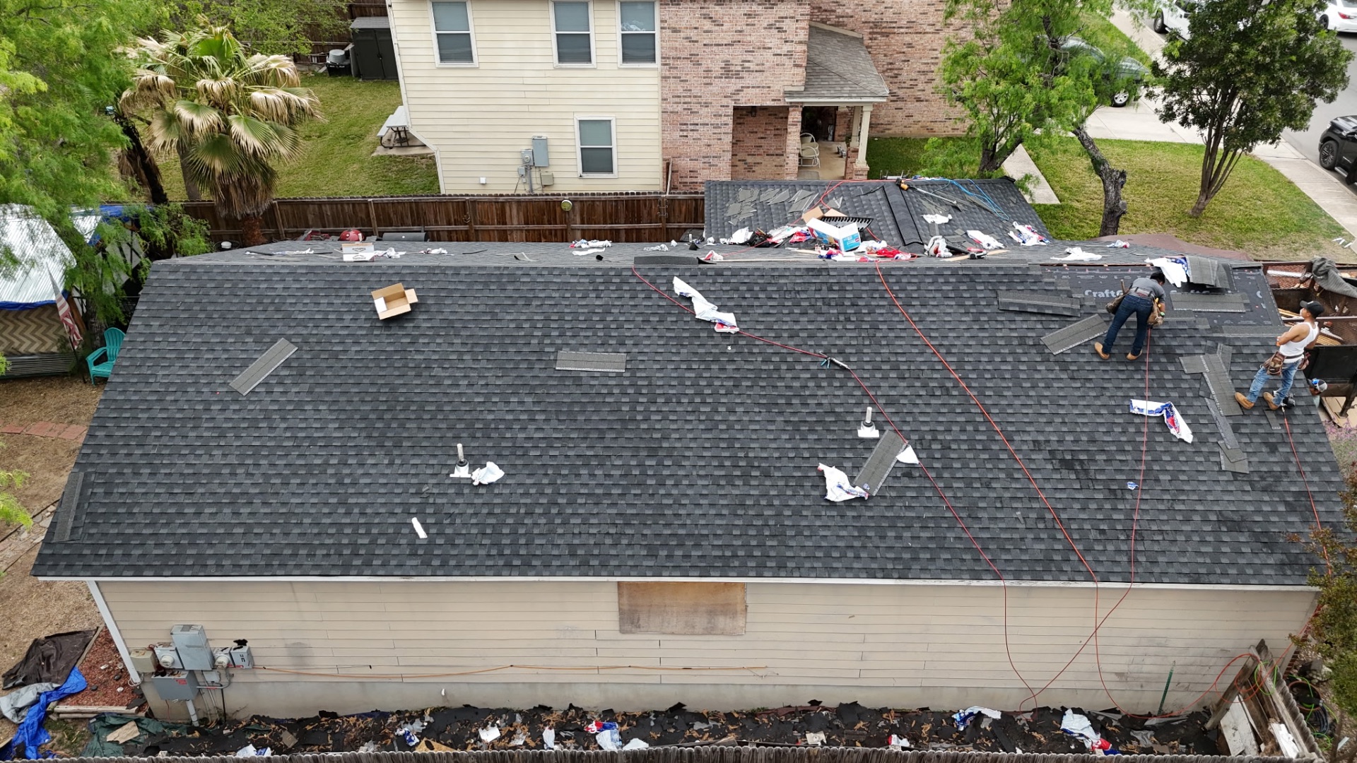 Rear drone view of new charcoal shingles being installed on West Side San Antonio home